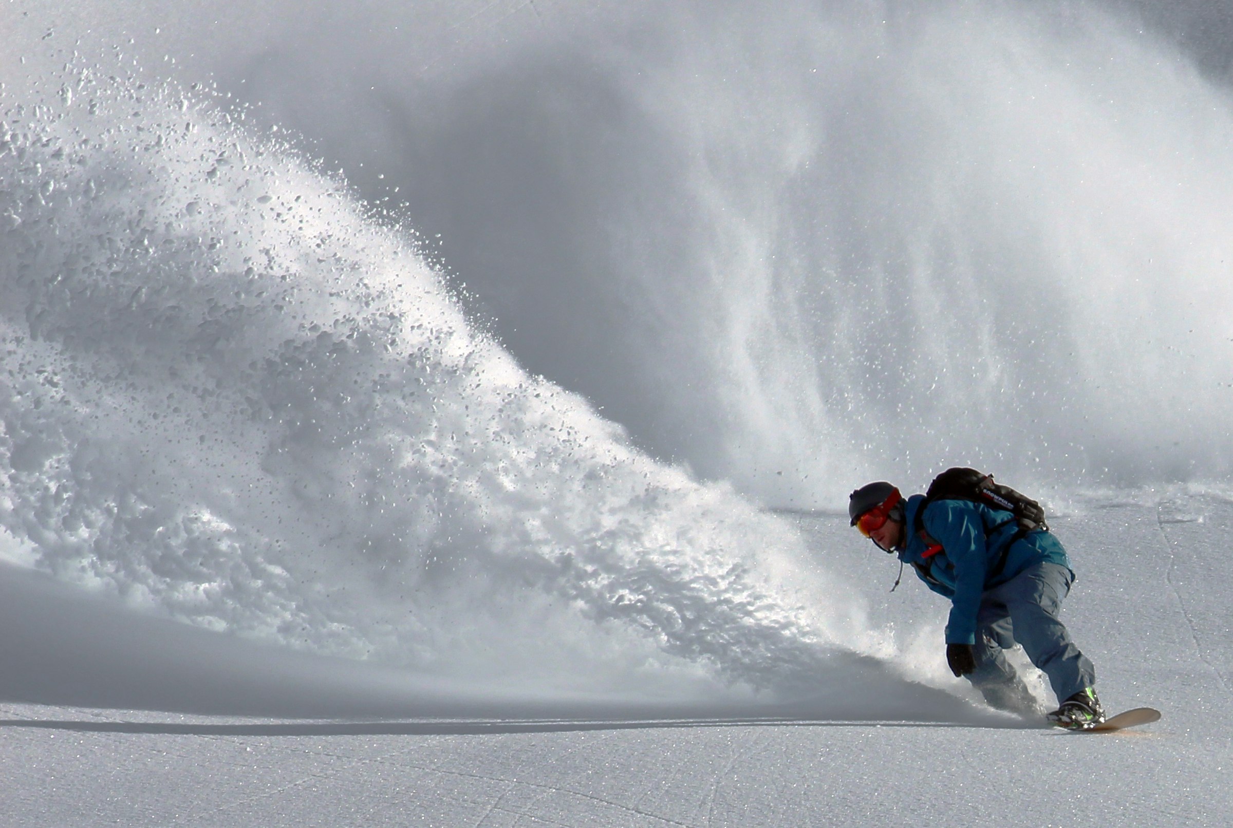 Snowboarder carving hard with a wave of powder arcing behind him
